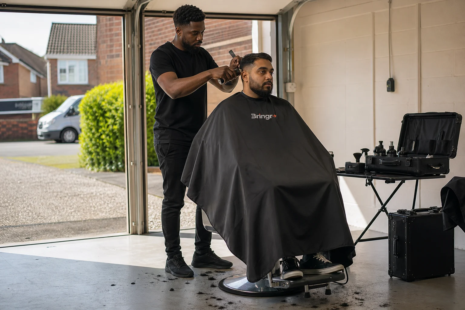 An independent mobile barber cutting a customer's hair in a clean residential garage